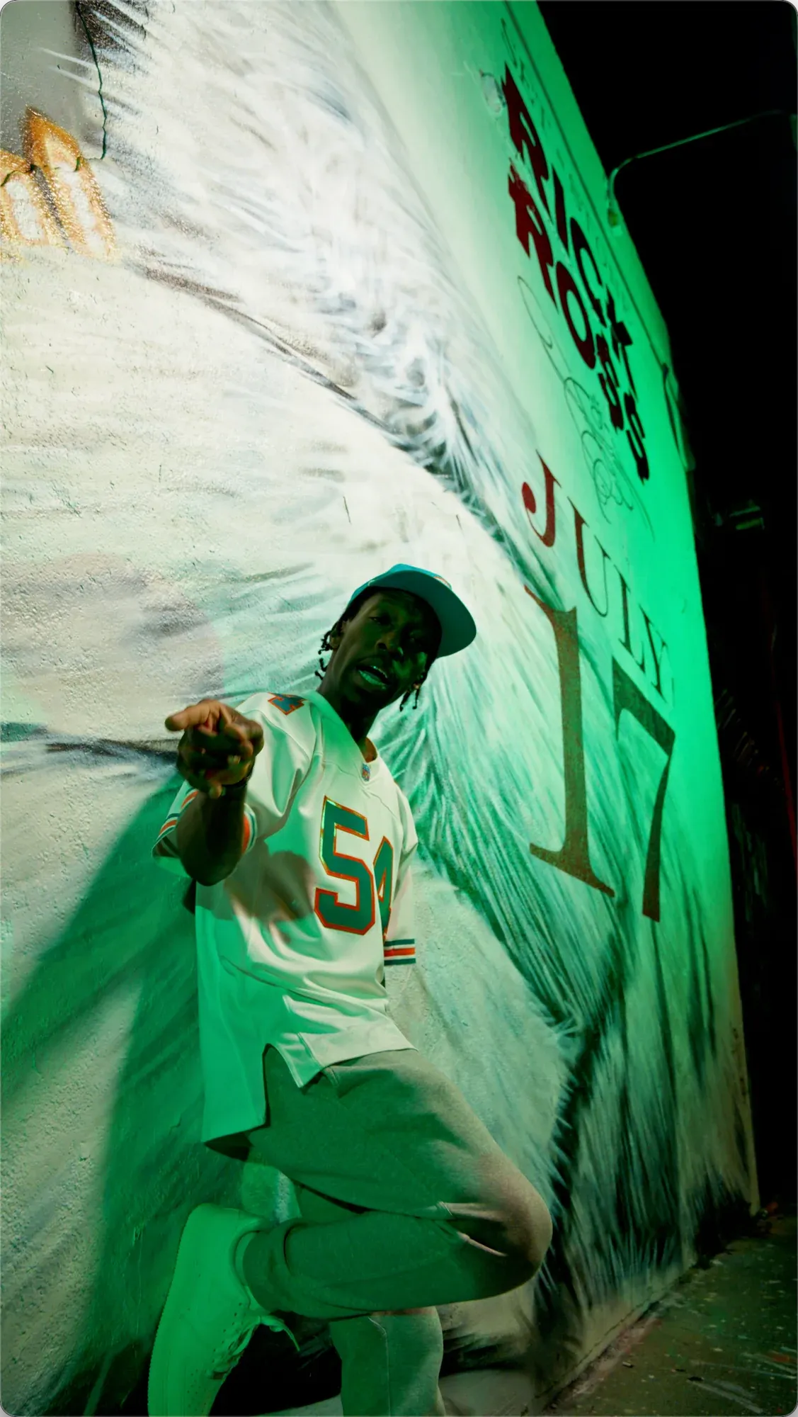 Low-angle view of INIKIO performing against the green-lit mural wall.